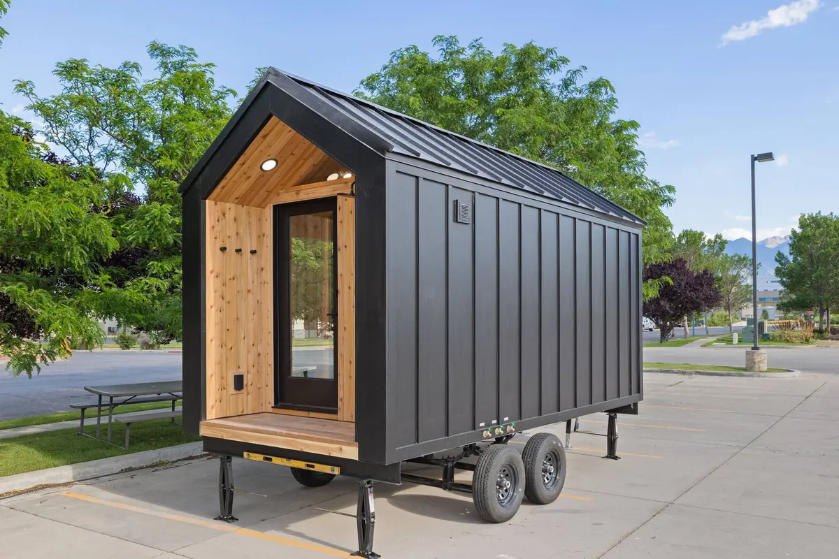 Black Sweaty Yeti modular sauna building with cedar entry and glass door sitting on a dual-axle transport trailer in a parking lot
