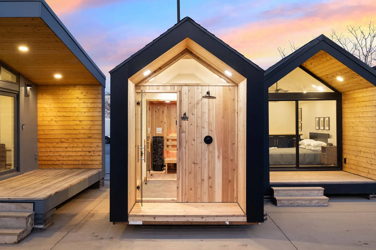 Sweaty Yeti modular sauna unit with black siding, cedar-lined front entry, glass door and small cedar deck, photographed at dusk between two other modular buildings