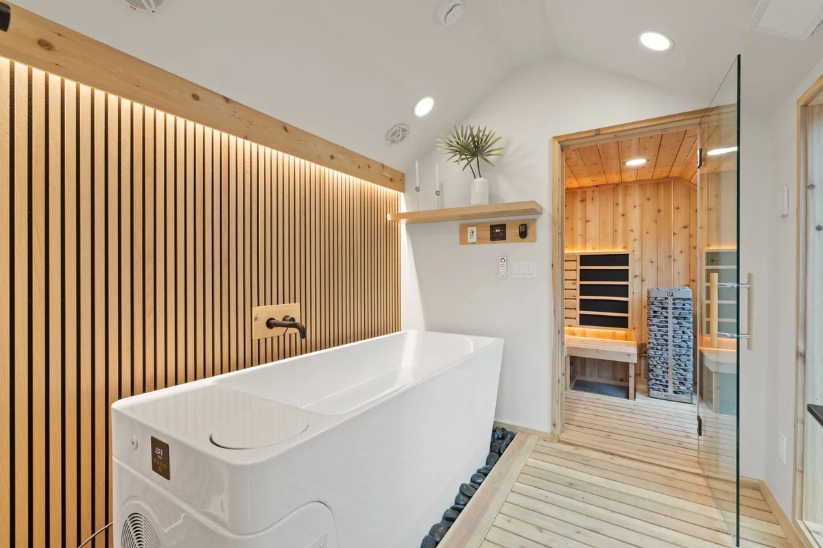 Sweaty Yeti cold plunge room with a white plunge tub, vertical wood slat accent wall with LED lighting, and a glass door into the cedar sauna